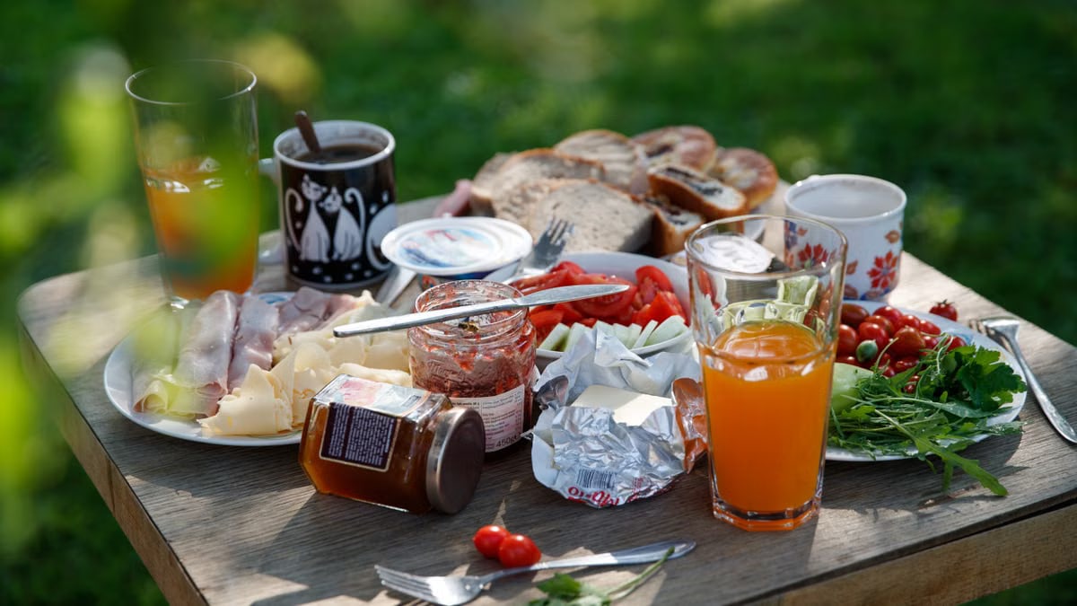 A delightful outdoor picnic table set with bread, cheese, meats, vegetables, and drinks, showcasing a lush summer setting.
