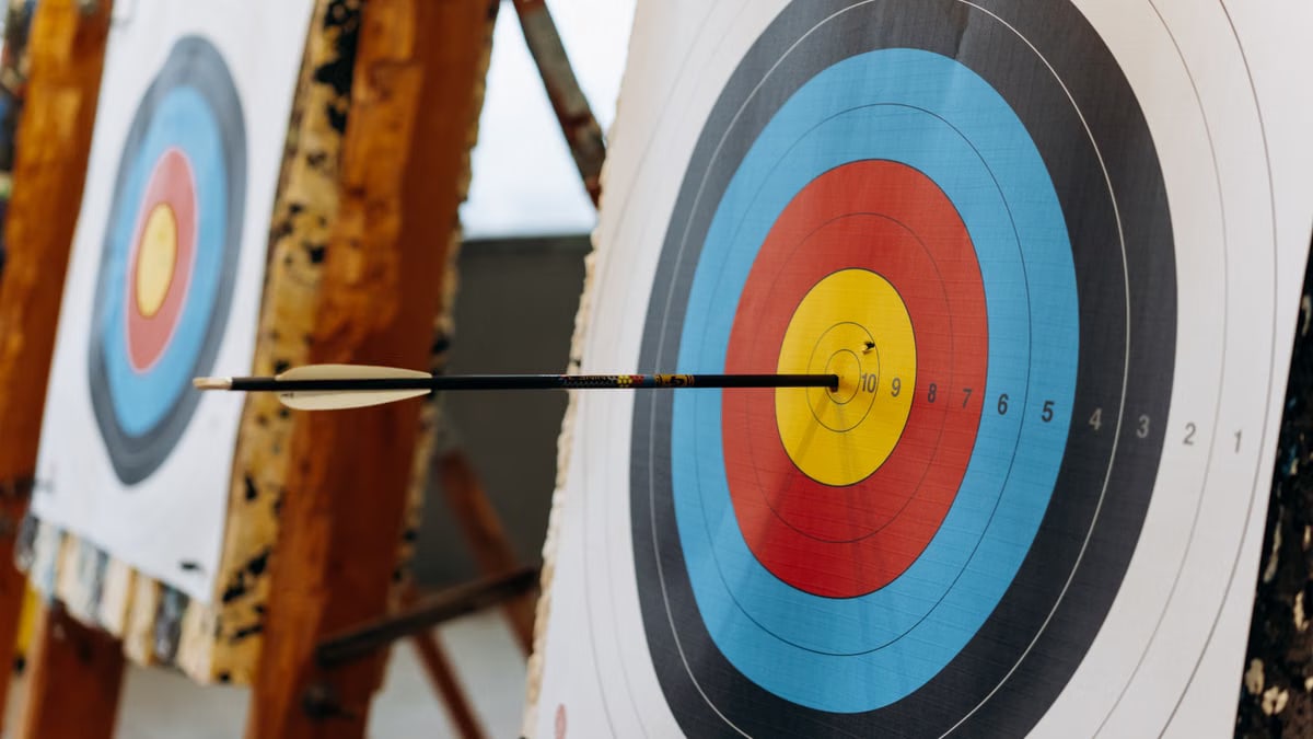 An arrow hits the bullseye on a colorful target in an indoor archery range.